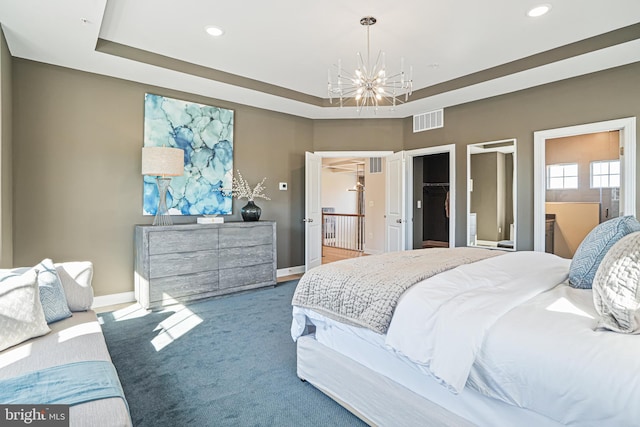 bedroom featuring ensuite bath, a spacious closet, a tray ceiling, a notable chandelier, and carpet floors