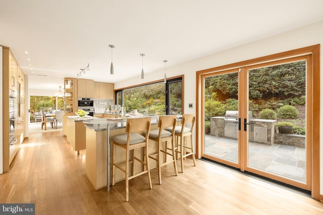 kitchen with light hardwood / wood-style floors, a wealth of natural light, light brown cabinets, and hanging light fixtures