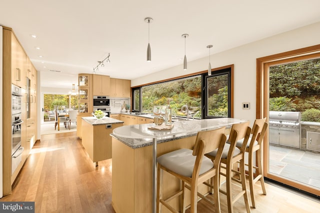 kitchen with light wood-type flooring, hanging light fixtures, plenty of natural light, and a kitchen island