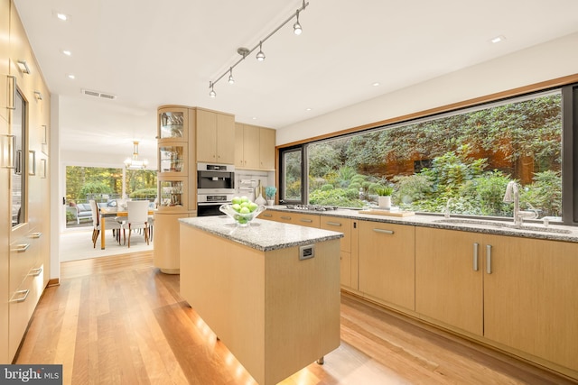 kitchen featuring light stone counters, a kitchen island, light brown cabinetry, light hardwood / wood-style floors, and sink