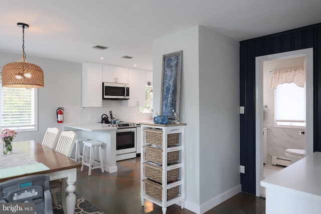 kitchen with hanging light fixtures, kitchen peninsula, a baseboard heating unit, white cabinetry, and appliances with stainless steel finishes