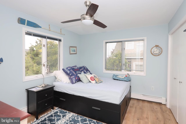 bedroom featuring light hardwood / wood-style flooring, a baseboard heating unit, a closet, and ceiling fan