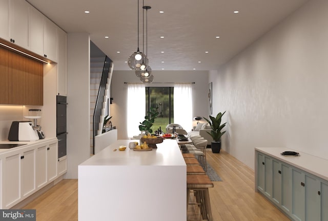 kitchen with a kitchen island, a kitchen bar, decorative light fixtures, light wood-type flooring, and white cabinetry