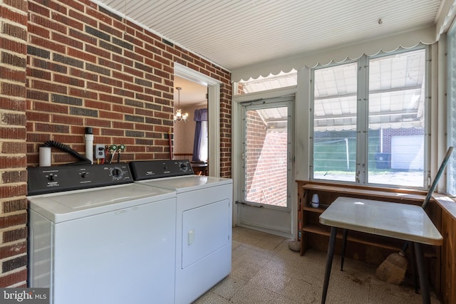 clothes washing area with an inviting chandelier, brick wall, and separate washer and dryer