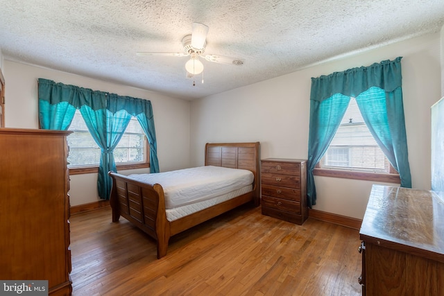 bedroom with multiple windows, wood-type flooring, a textured ceiling, and ceiling fan