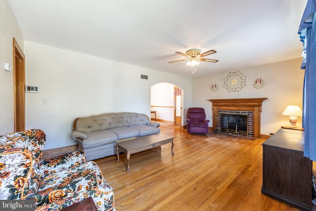 living room with light wood-type flooring, ceiling fan, and a fireplace