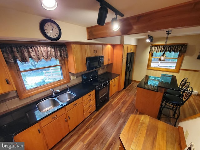 kitchen featuring dark countertops, wood finished floors, a sink, black appliances, and backsplash