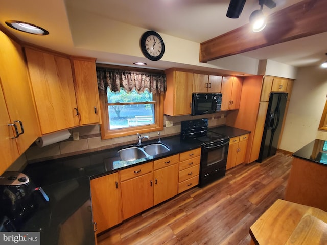 kitchen with dark countertops, tasteful backsplash, a sink, black appliances, and light wood finished floors
