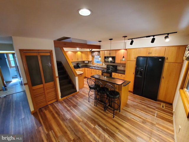 kitchen with dark countertops, rail lighting, a sink, black appliances, and light wood-style flooring