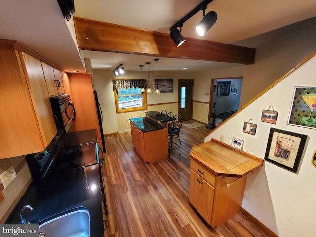 kitchen with black range, a center island, hanging light fixtures, hardwood / wood-style flooring, and a breakfast bar