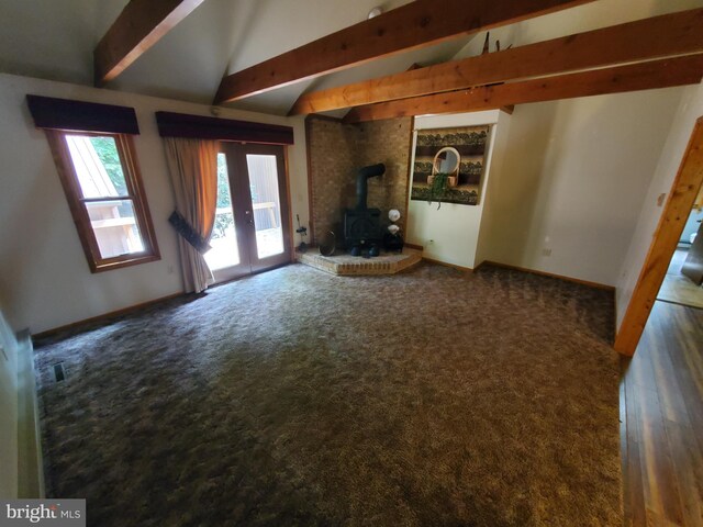 unfurnished living room featuring a wood stove, french doors, lofted ceiling with beams, and dark carpet