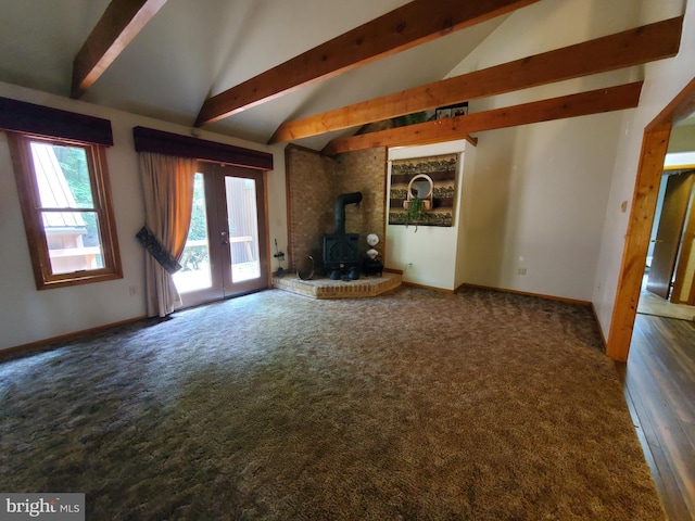 unfurnished living room with a wood stove, carpet flooring, baseboards, and lofted ceiling with beams