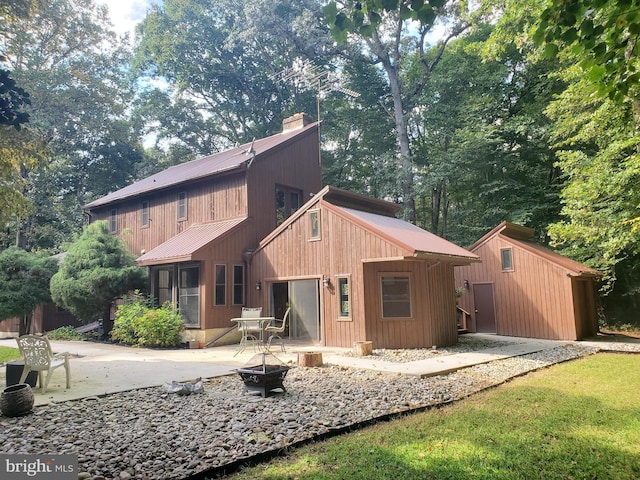 rear view of property featuring a chimney, a patio, an outdoor fire pit, and metal roof