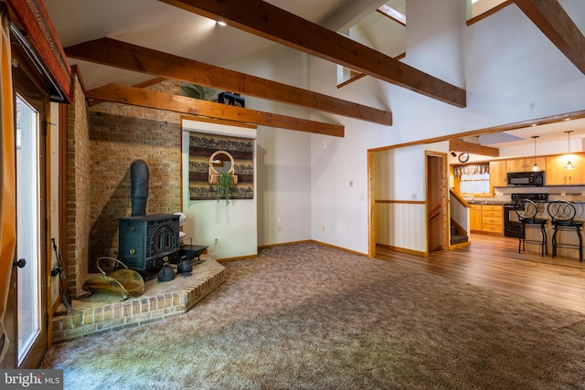 unfurnished living room with a wood stove, hardwood / wood-style floors, beam ceiling, and high vaulted ceiling