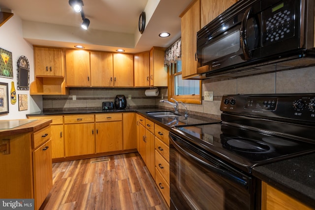 kitchen with light hardwood / wood-style floors, tasteful backsplash, black appliances, and sink