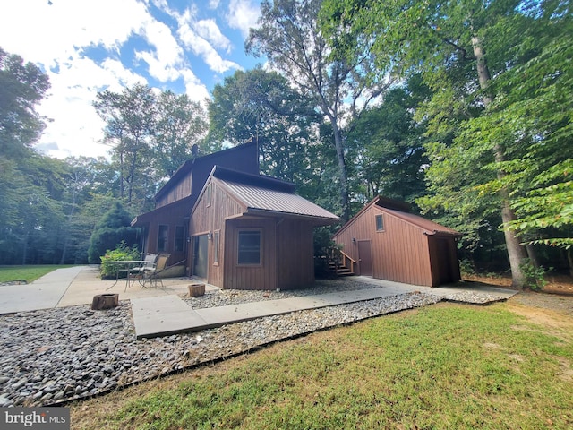 view of side of home featuring board and batten siding, a patio area, an outbuilding, a lawn, and metal roof