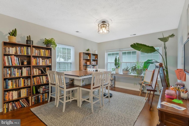 dining space with a textured ceiling, a healthy amount of sunlight, and dark wood-type flooring