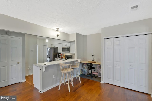 kitchen featuring dark hardwood / wood-style floors, white cabinets, kitchen peninsula, a kitchen breakfast bar, and stainless steel appliances