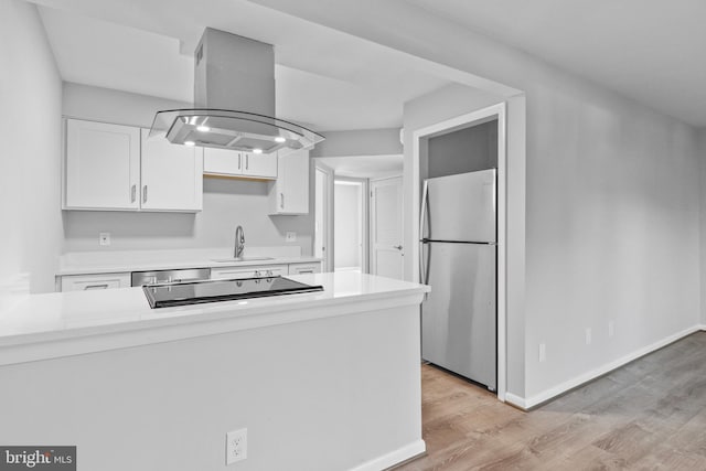 kitchen with white cabinets, sink, island exhaust hood, appliances with stainless steel finishes, and light hardwood / wood-style floors