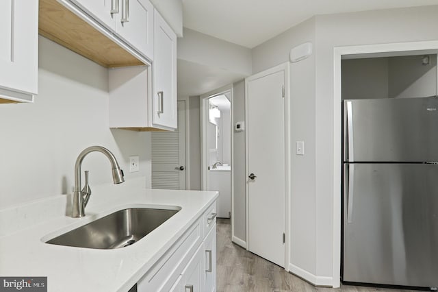 kitchen with white cabinetry, sink, and stainless steel refrigerator