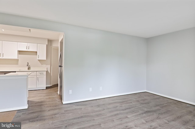 interior space with white cabinets, light hardwood / wood-style floors, stainless steel fridge, and sink