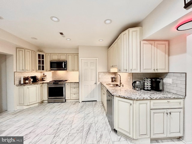 kitchen featuring light stone counters, stainless steel appliances, sink, and decorative backsplash