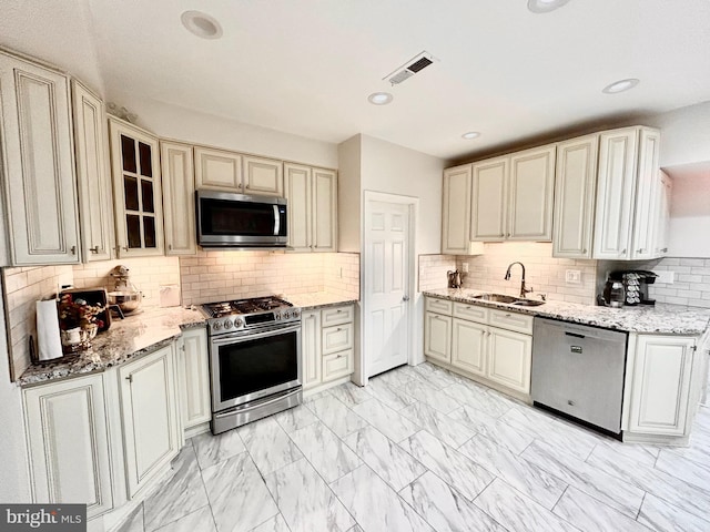 kitchen featuring light stone countertops, cream cabinets, appliances with stainless steel finishes, and sink