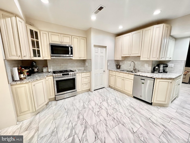 kitchen featuring light stone counters, sink, cream cabinetry, stainless steel appliances, and decorative backsplash