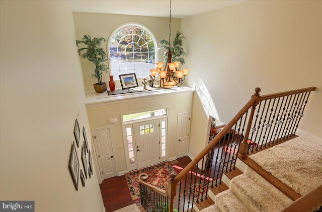 foyer entrance featuring wood finished floors, a towering ceiling, baseboards, stairs, and an inviting chandelier