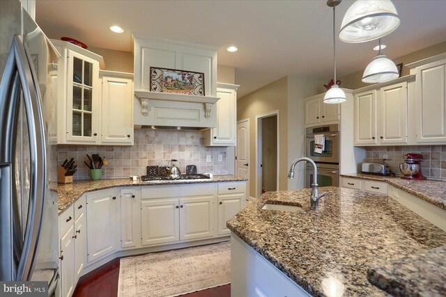 kitchen featuring glass insert cabinets, appliances with stainless steel finishes, a sink, white cabinetry, and backsplash