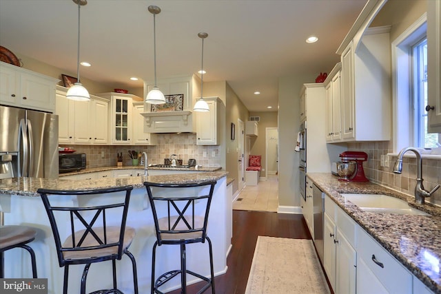 kitchen with appliances with stainless steel finishes, stone countertops, white cabinetry, a sink, and a kitchen breakfast bar