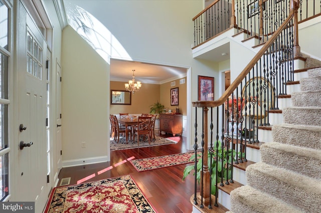 entrance foyer with visible vents, a high ceiling, ornamental molding, wood finished floors, and a chandelier