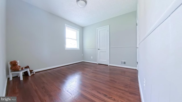 empty room with dark wood-type flooring, a textured ceiling, and lofted ceiling