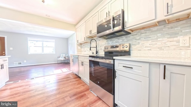 kitchen with tasteful backsplash, sink, light wood-type flooring, stainless steel appliances, and white cabinets