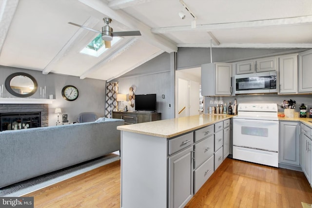 kitchen with ceiling fan, white electric range oven, a fireplace, lofted ceiling with skylight, and light wood-type flooring