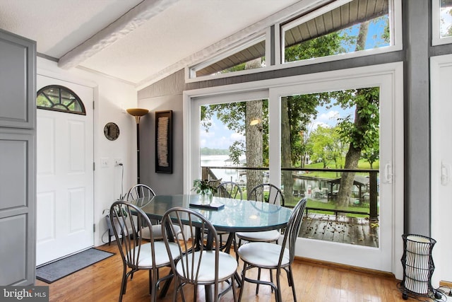 dining area with a water view, light wood-type flooring, and vaulted ceiling with beams