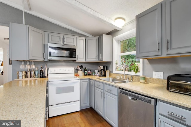 kitchen with lofted ceiling, sink, gray cabinets, stainless steel appliances, and light hardwood / wood-style floors