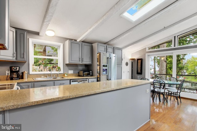 kitchen with appliances with stainless steel finishes, a wealth of natural light, sink, and vaulted ceiling with skylight