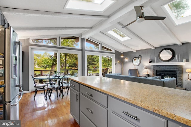 kitchen featuring a glass covered fireplace, light wood-type flooring, gray cabinets, vaulted ceiling with skylight, and ceiling fan