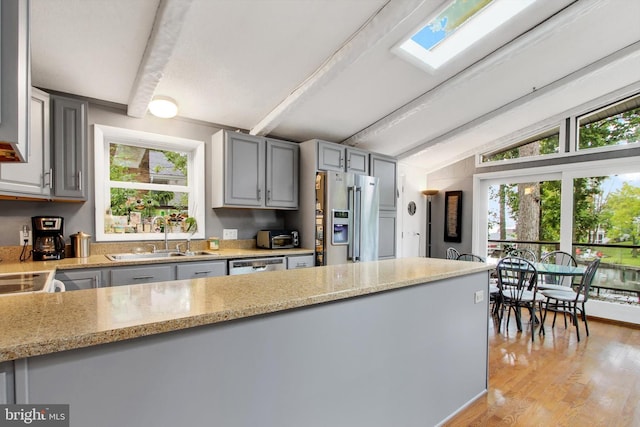 kitchen with dishwashing machine, light stone counters, a sink, vaulted ceiling with beams, and high end fridge