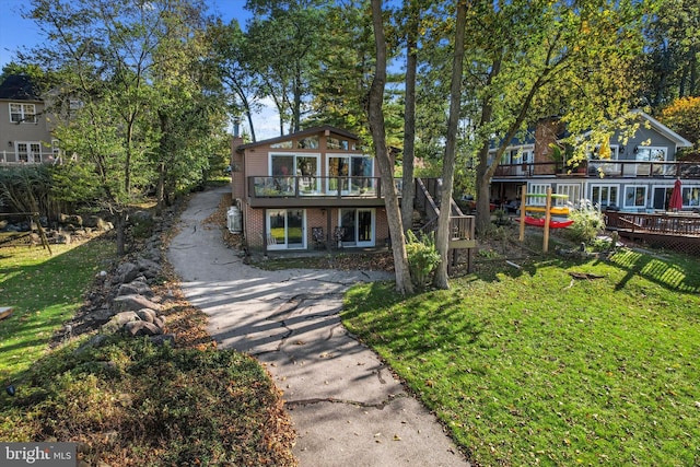 view of front facade featuring brick siding, driveway, a wooden deck, and a front lawn