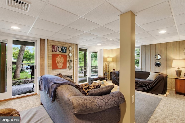 living room featuring light carpet, a paneled ceiling, wood walls, and plenty of natural light