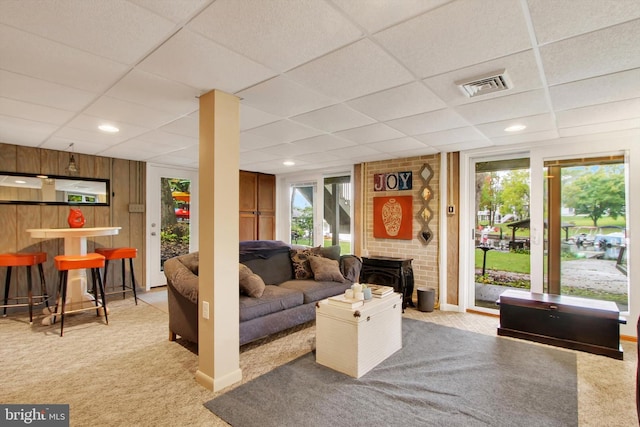 carpeted living room with a brick fireplace, a drop ceiling, plenty of natural light, and indoor bar