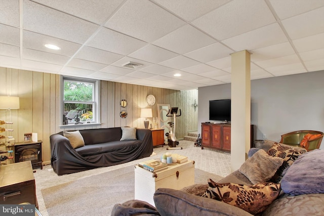 carpeted living room featuring a paneled ceiling, wooden walls, and a wood stove