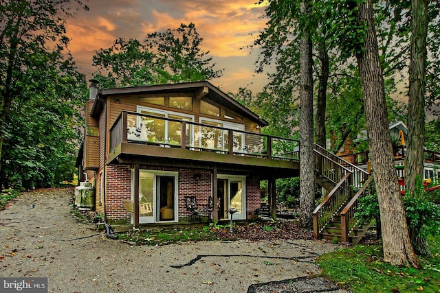 back of property at dusk with a deck, stairway, and brick siding