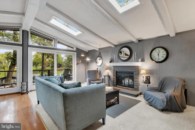 living area featuring hardwood / wood-style flooring, a stone fireplace, and lofted ceiling with skylight