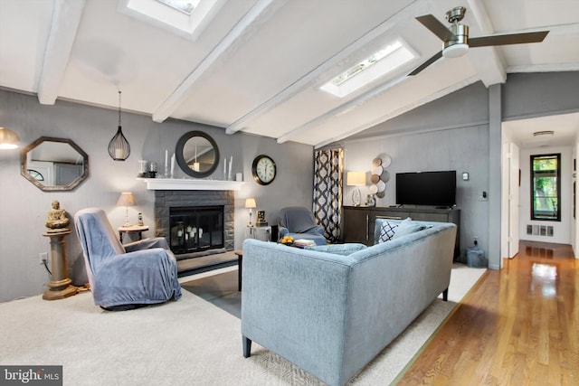 living area with visible vents, vaulted ceiling with skylight, a ceiling fan, a fireplace, and wood finished floors