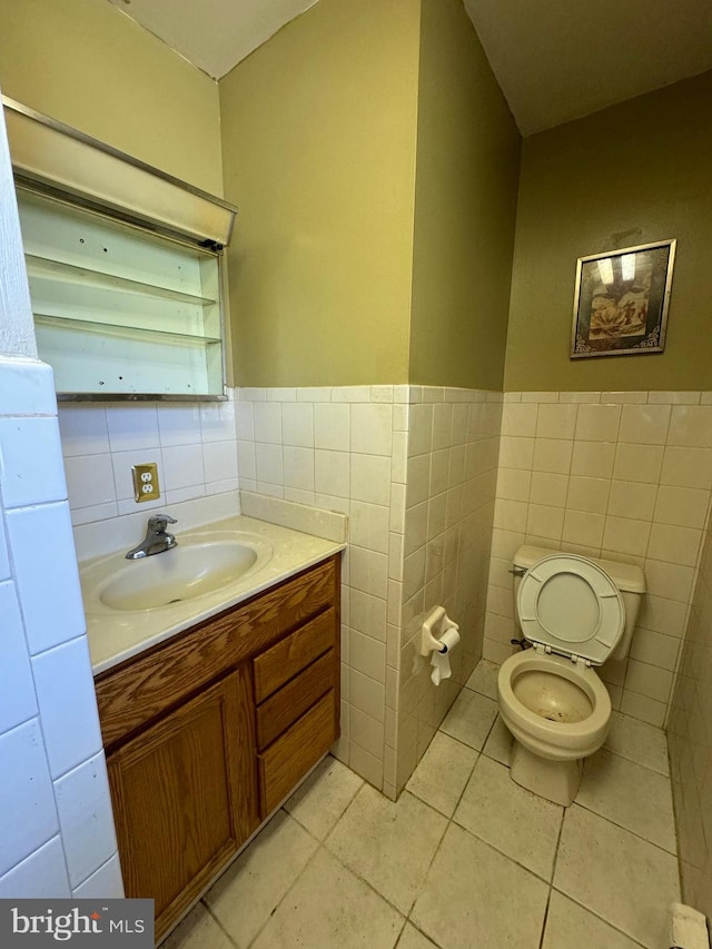 bathroom with toilet, vanity, tile patterned floors, and tile walls