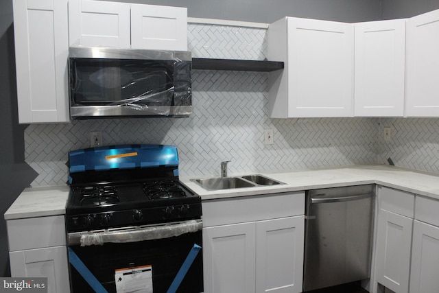 kitchen featuring appliances with stainless steel finishes, white cabinetry, light stone counters, tasteful backsplash, and sink