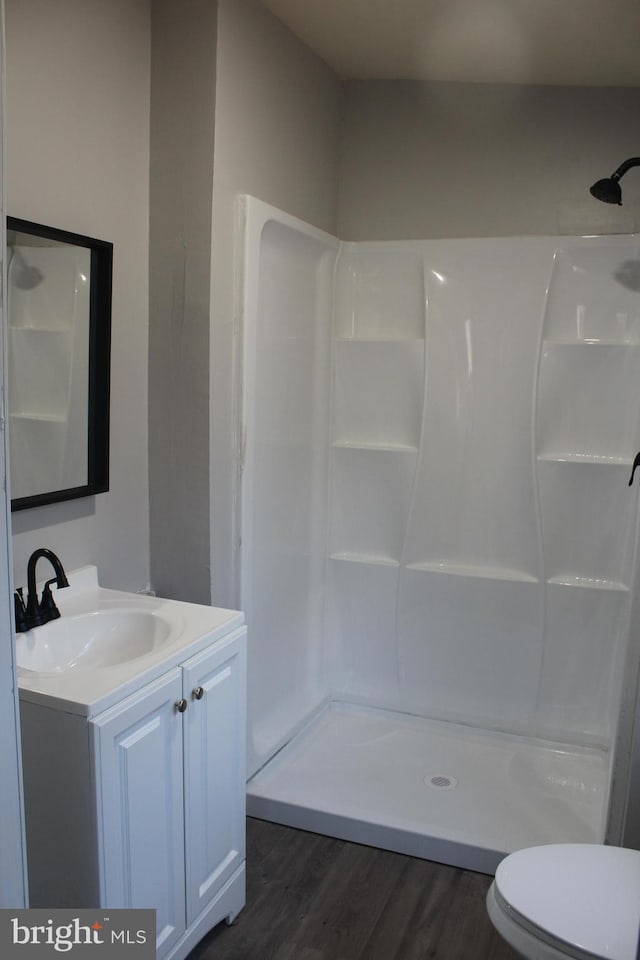 bathroom featuring hardwood / wood-style floors, walk in shower, vanity, and toilet